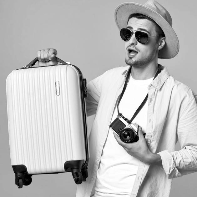 Young man with a tourist appearance holding a cabin suitcase, representing the Lock & Relax luggage storage service for compact suitcases in Malaga.