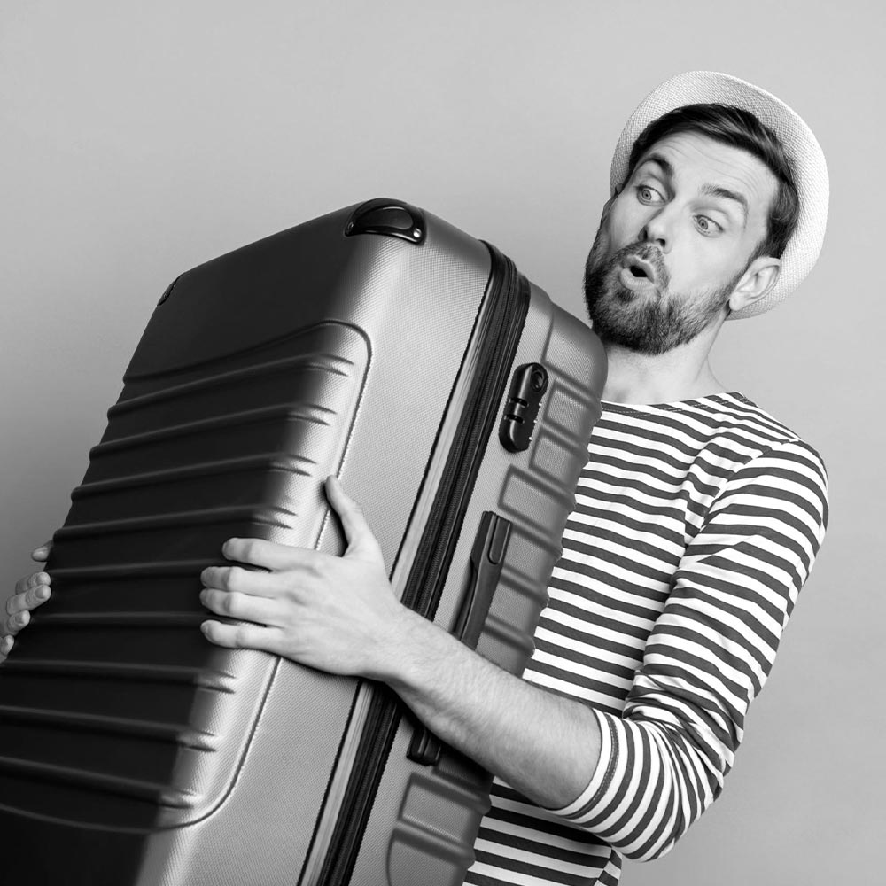 Young man holding a large suitcase with effort, illustrating the luggage storage solutions for bulky suitcases from Lock & Relax in Malaga.